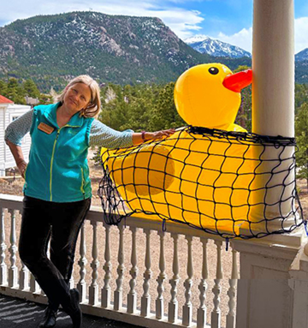 stanley home museum docent standing next to an inflatable duck for the estes park rotary club duck race festival