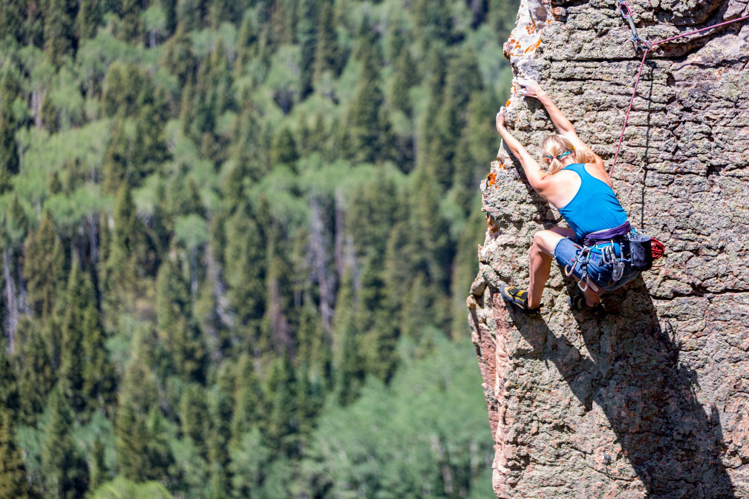 Caucasian female athletic blond rock climber on the sheer face of a granite cliff reaching up with her hands to gain more heights.  